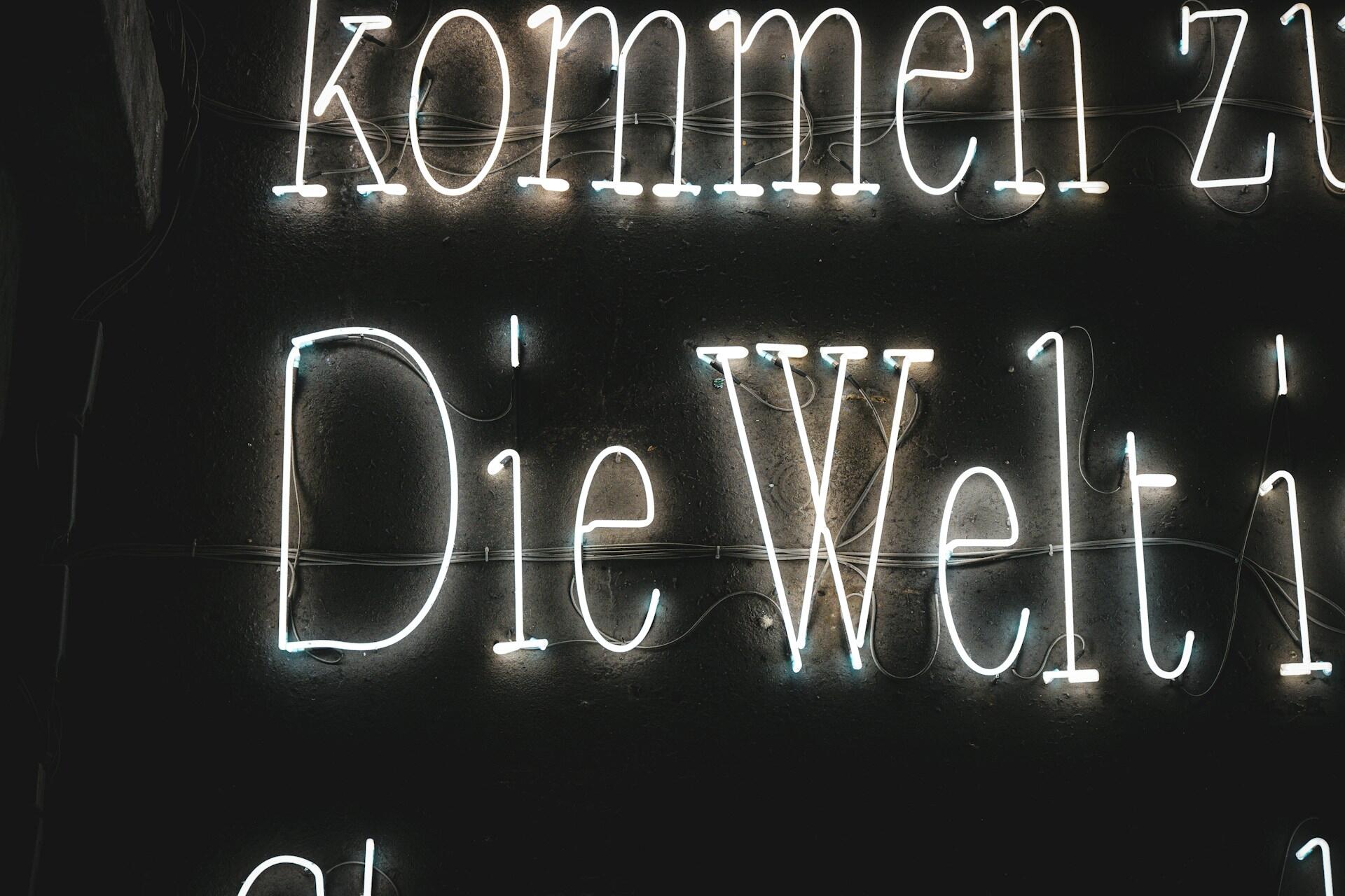 White neon letters spelling part of a German phrase on a dark wall.