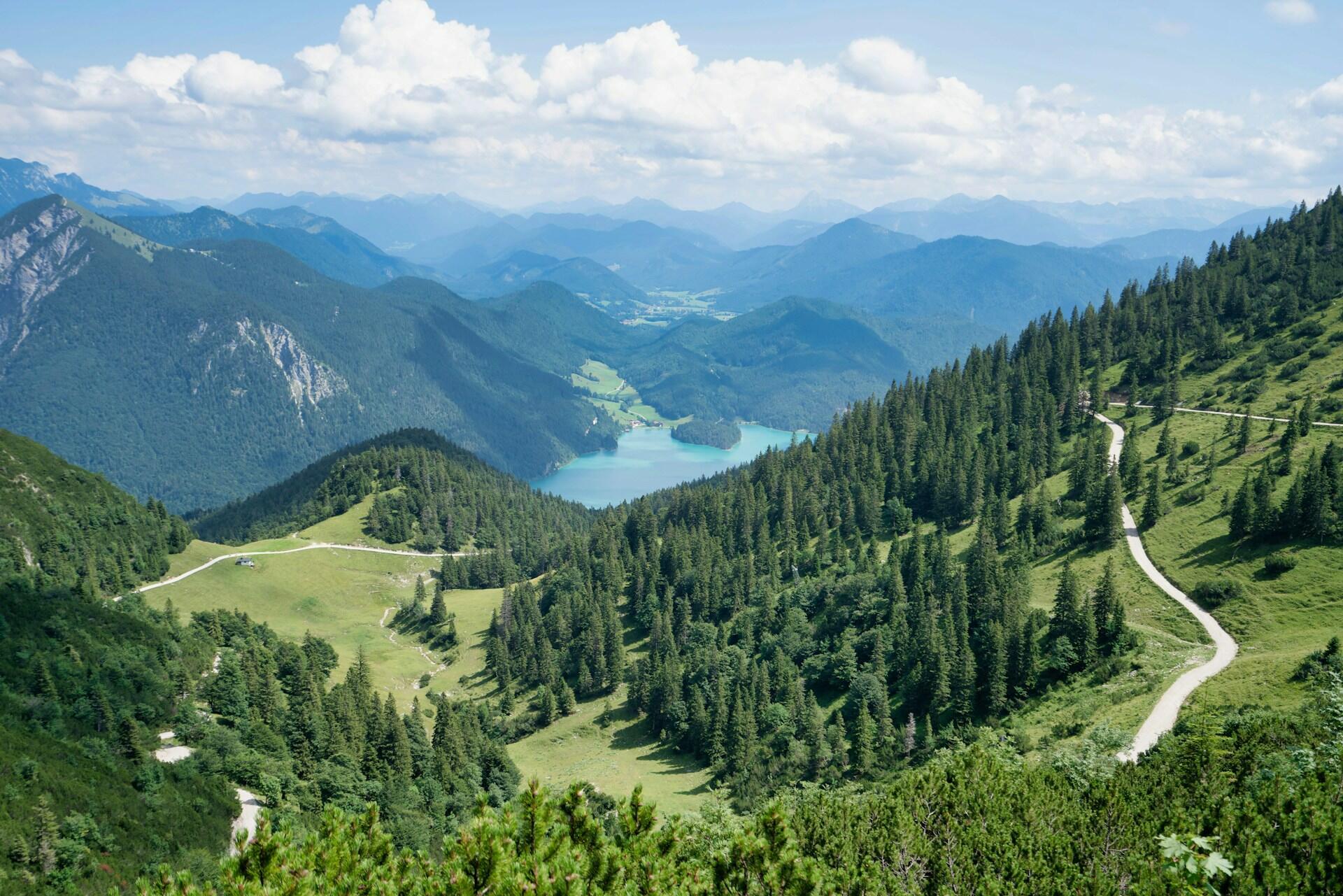 Green mountain landscape with forests, lake, clouds, and winding paths
