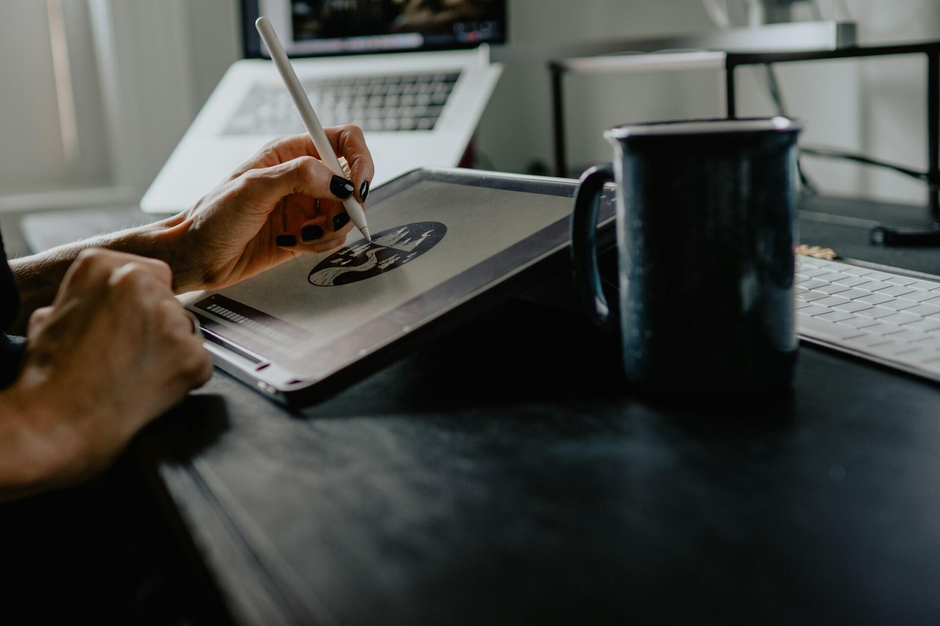 Designer using a stylus and drawing tablet beside a laptop and mug