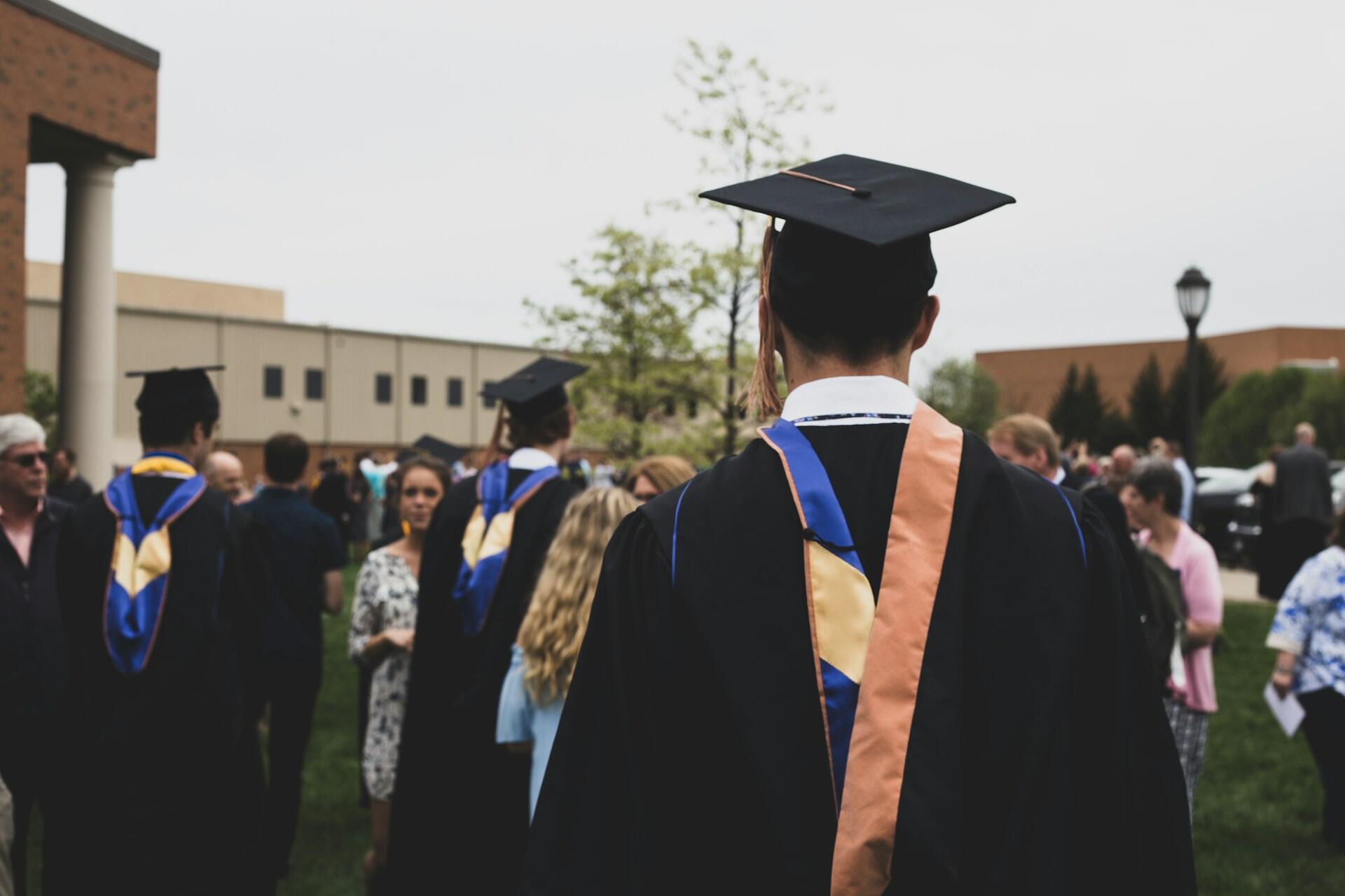 Graduate in a cap and gown standing outside among people