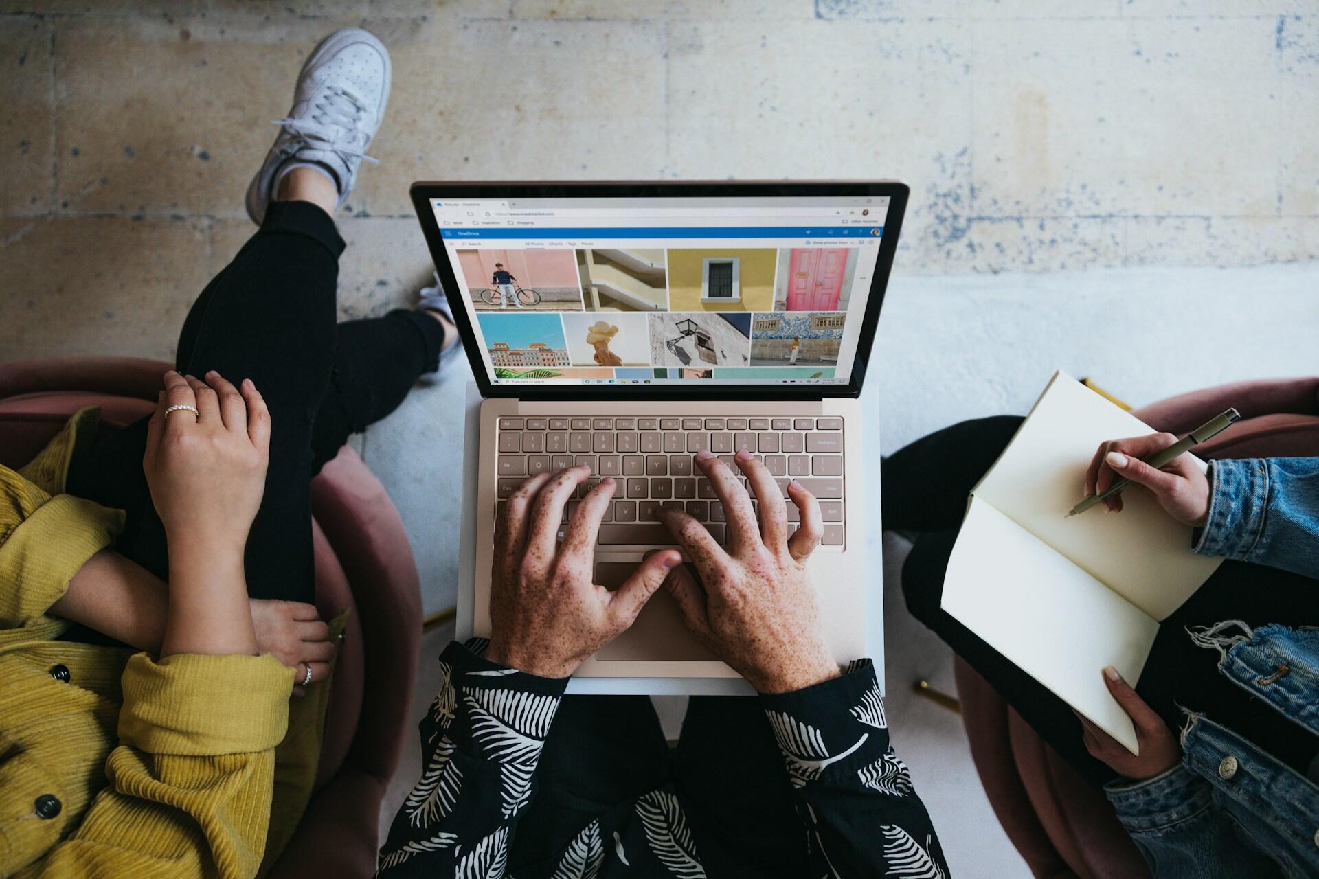 Two people reviewing visual work on a laptop and taking notes