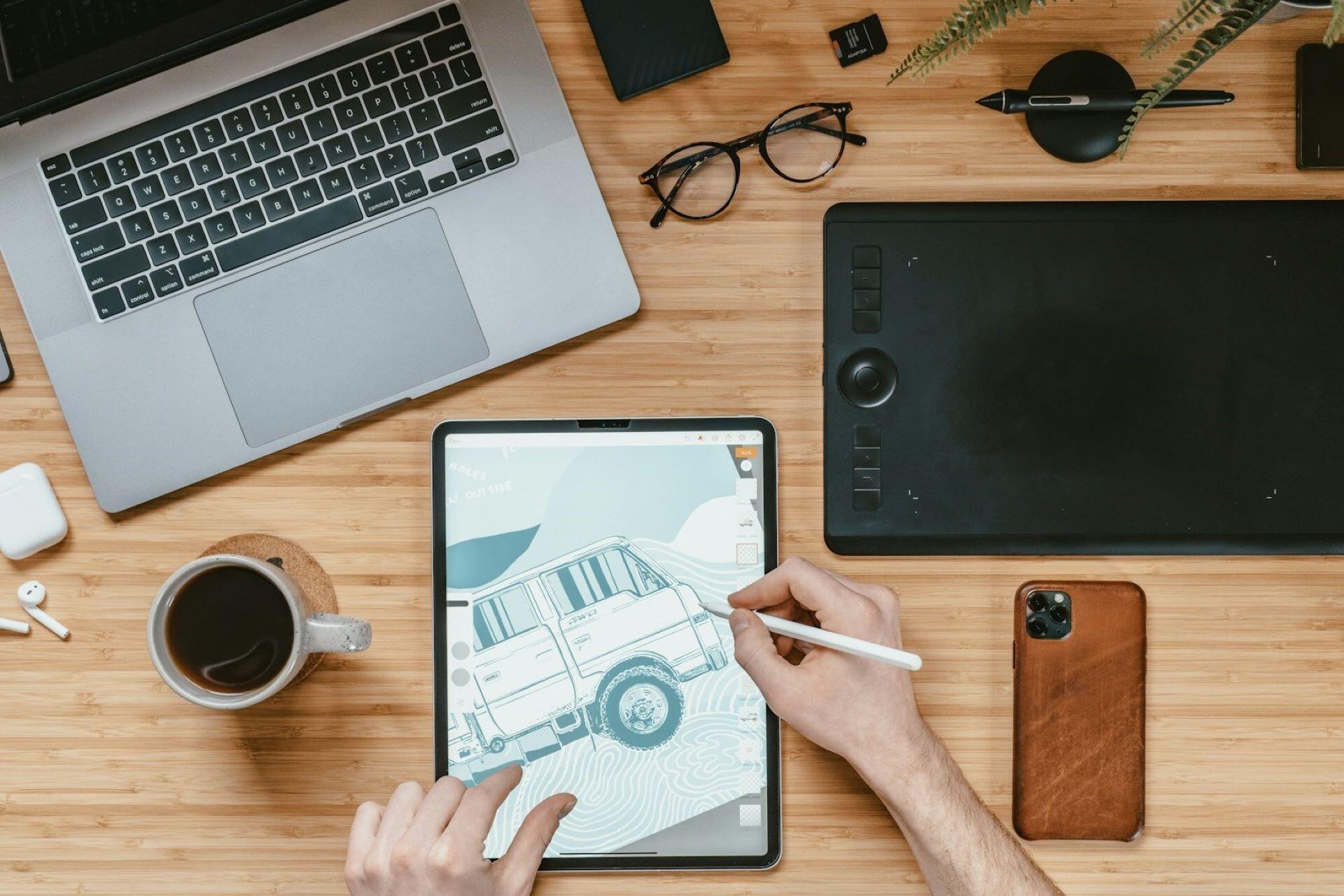 Designer sketching a digital illustration on a tablet beside a laptop and graphics tablet