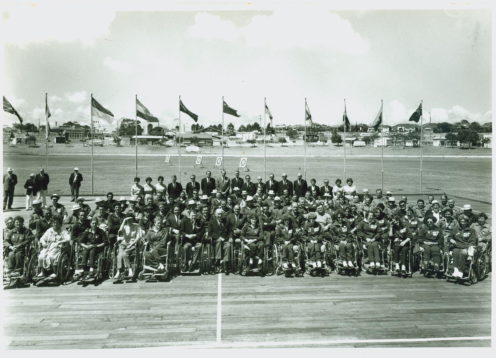 A team of wheelchair athletes posed on a sports track with flags flying in the background.