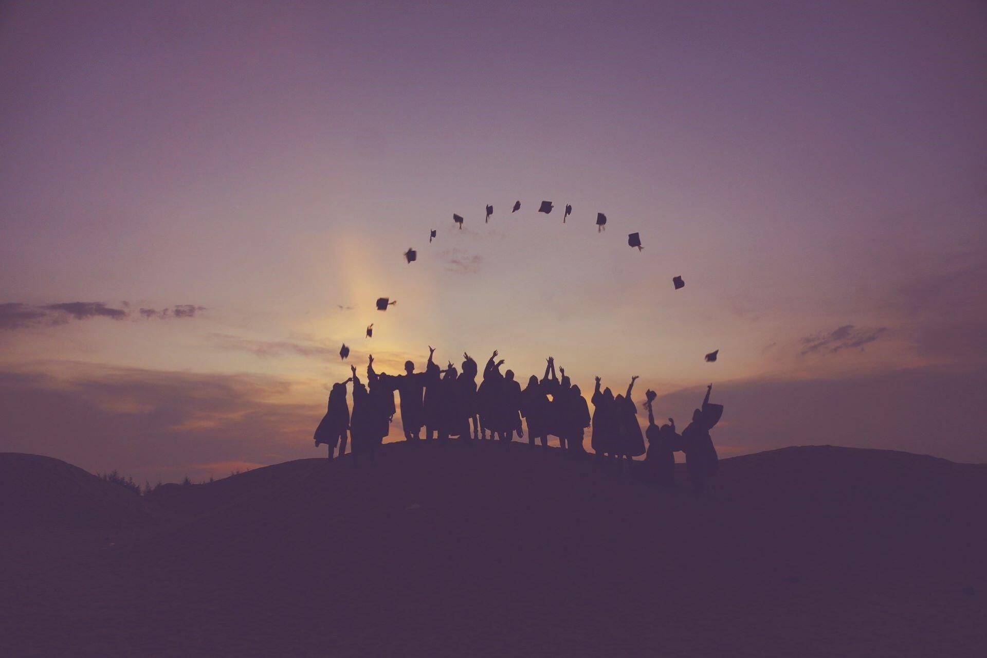 Silhouetted graduates throwing caps into the air at sunset