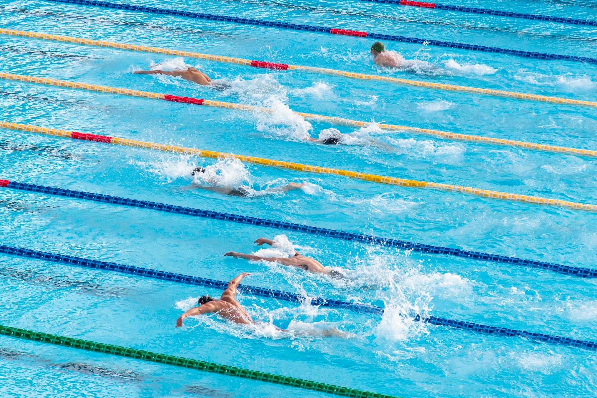 An aerial view of a swimming pool with lanes marked by yellow buoys and a swimmer in each lane.