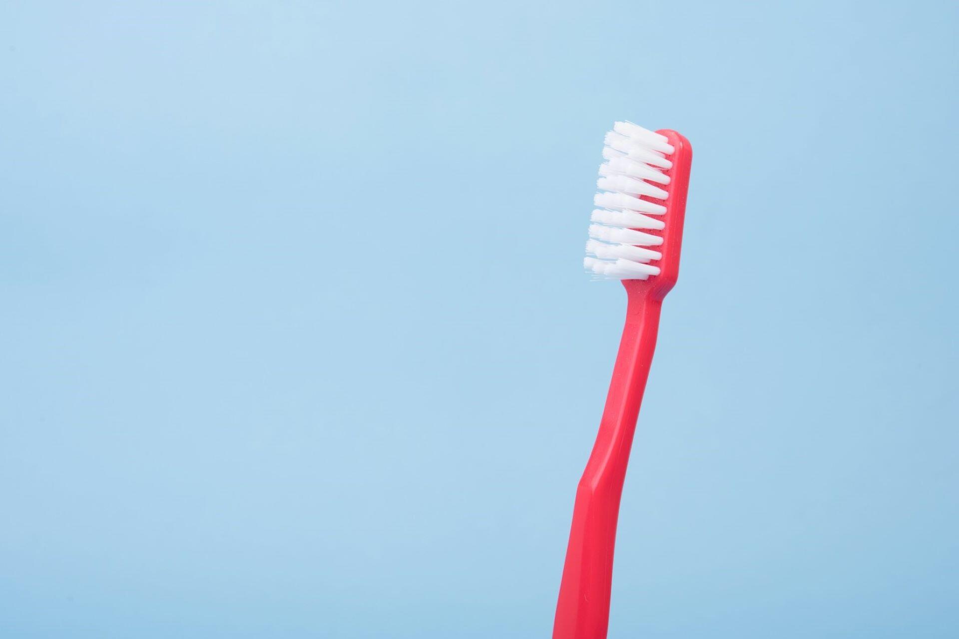 Red toothbrush with white bristles on a light blue background.