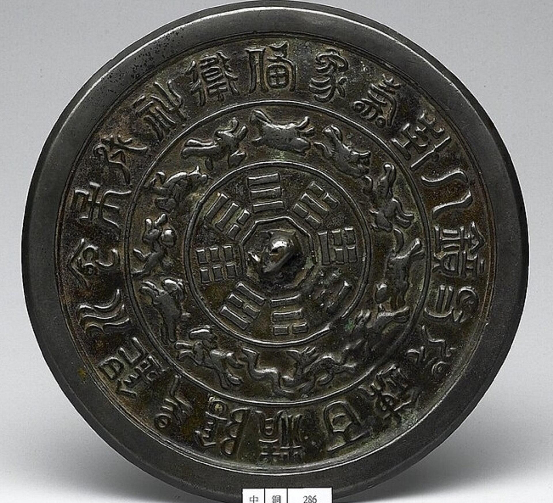 A bronze circular icon with many relief engravings on its face.
