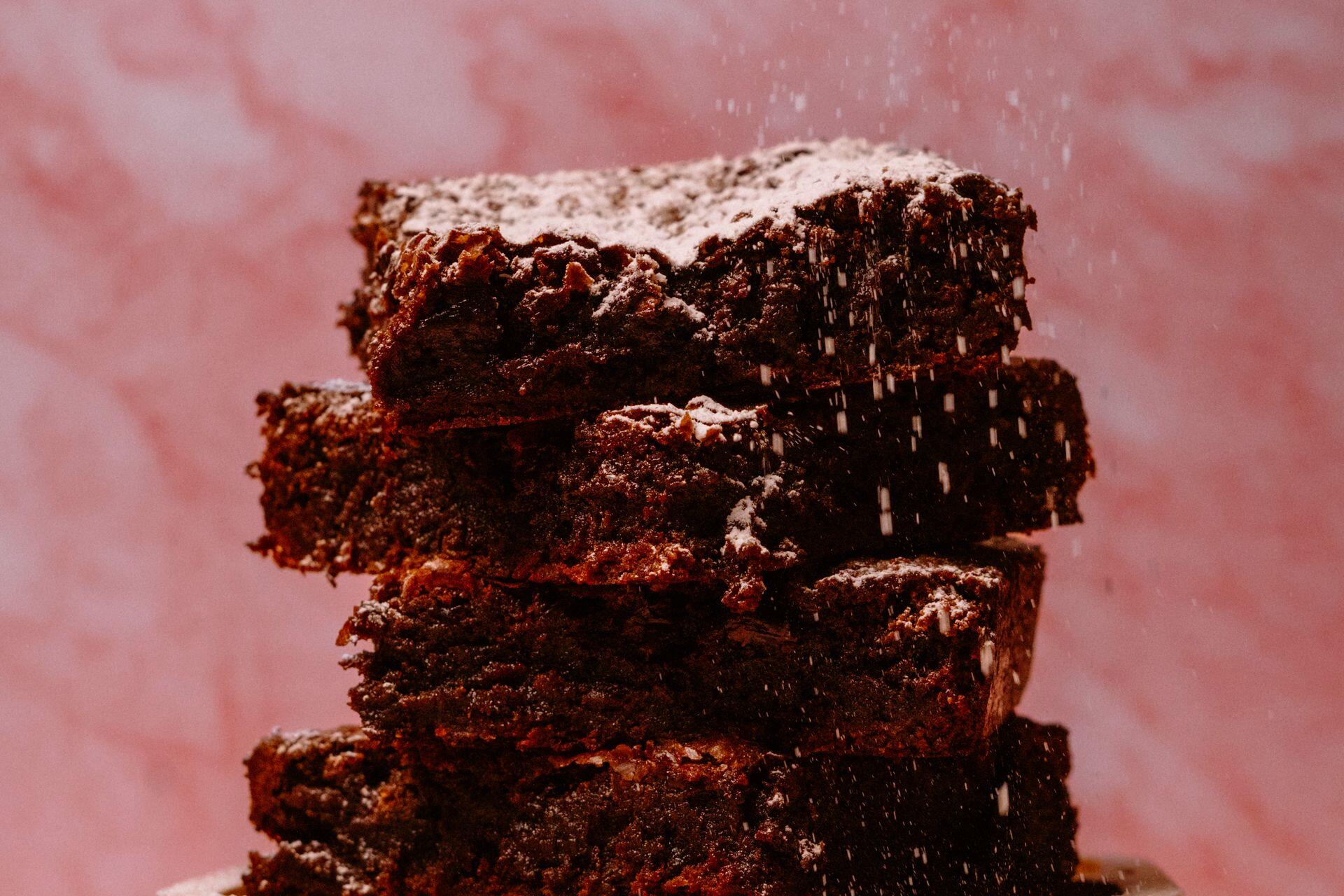 Stack of chocolate brownies dusted with powdered sugar against a pink textured background.