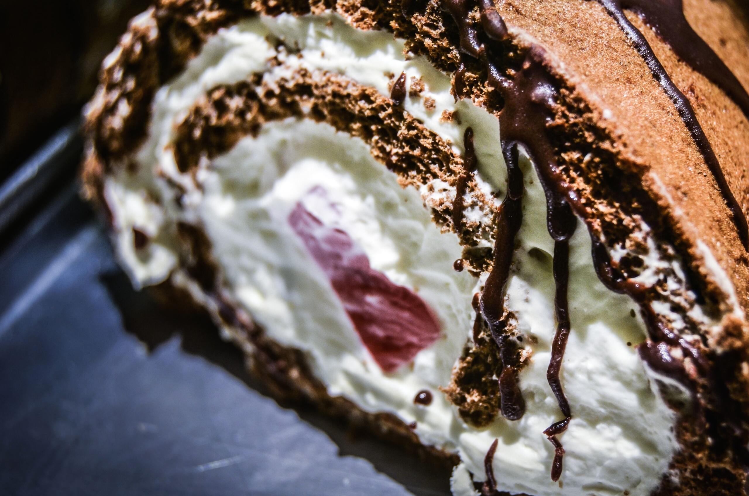 Close-up of a chocolate roll cake filled with whipped cream and a pink filling, drizzled with chocolate sauce.
