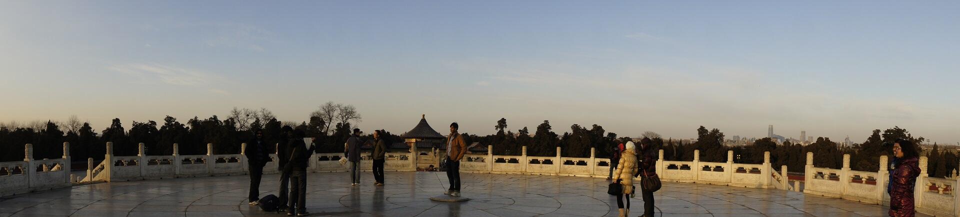 People stand on a raised platform surrounded by a low white bordering wall and featuring a raised centre stone with tiles laid in precise measure.