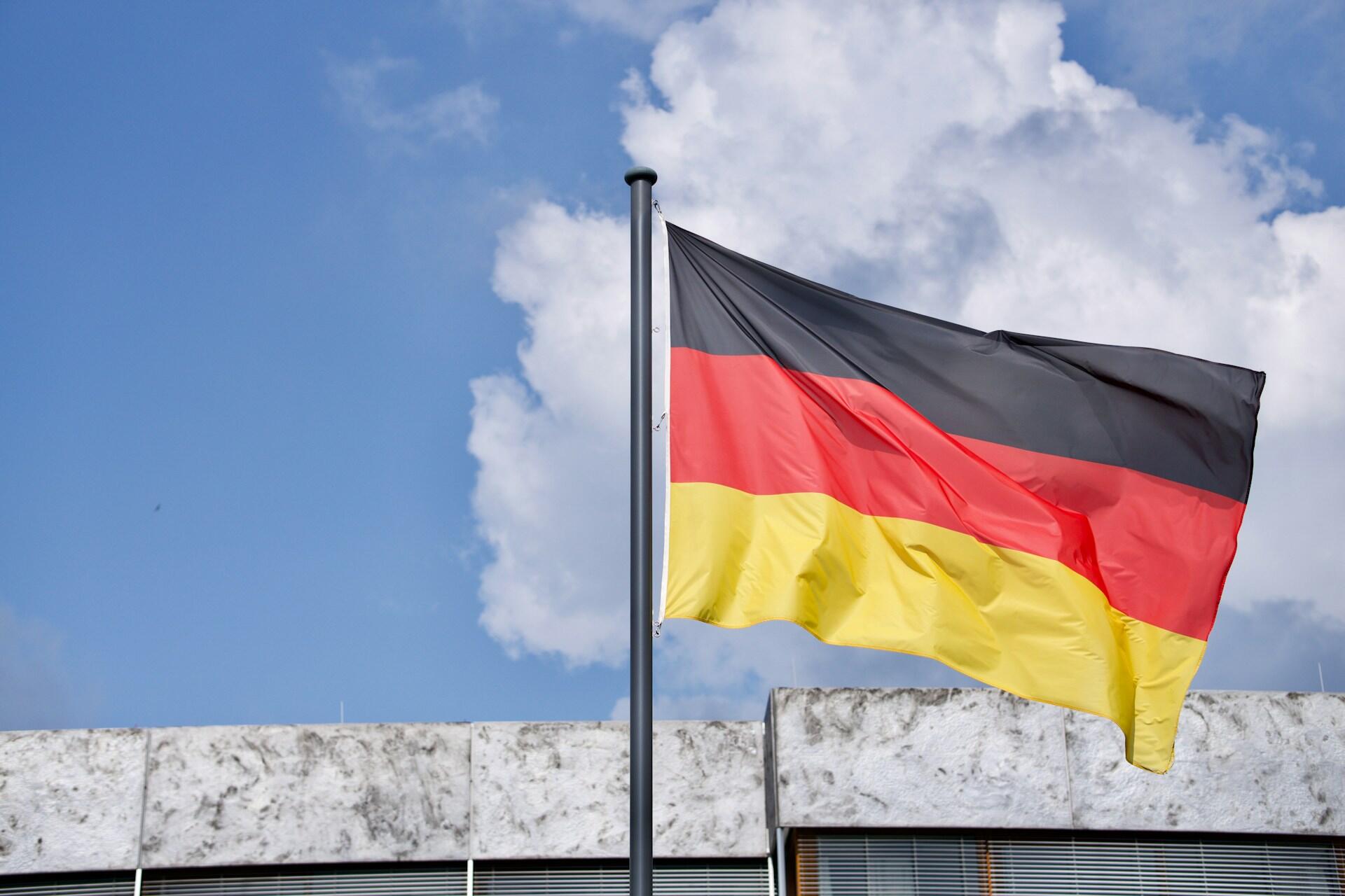 German flag flying on a flagpole against a blue sky with clouds