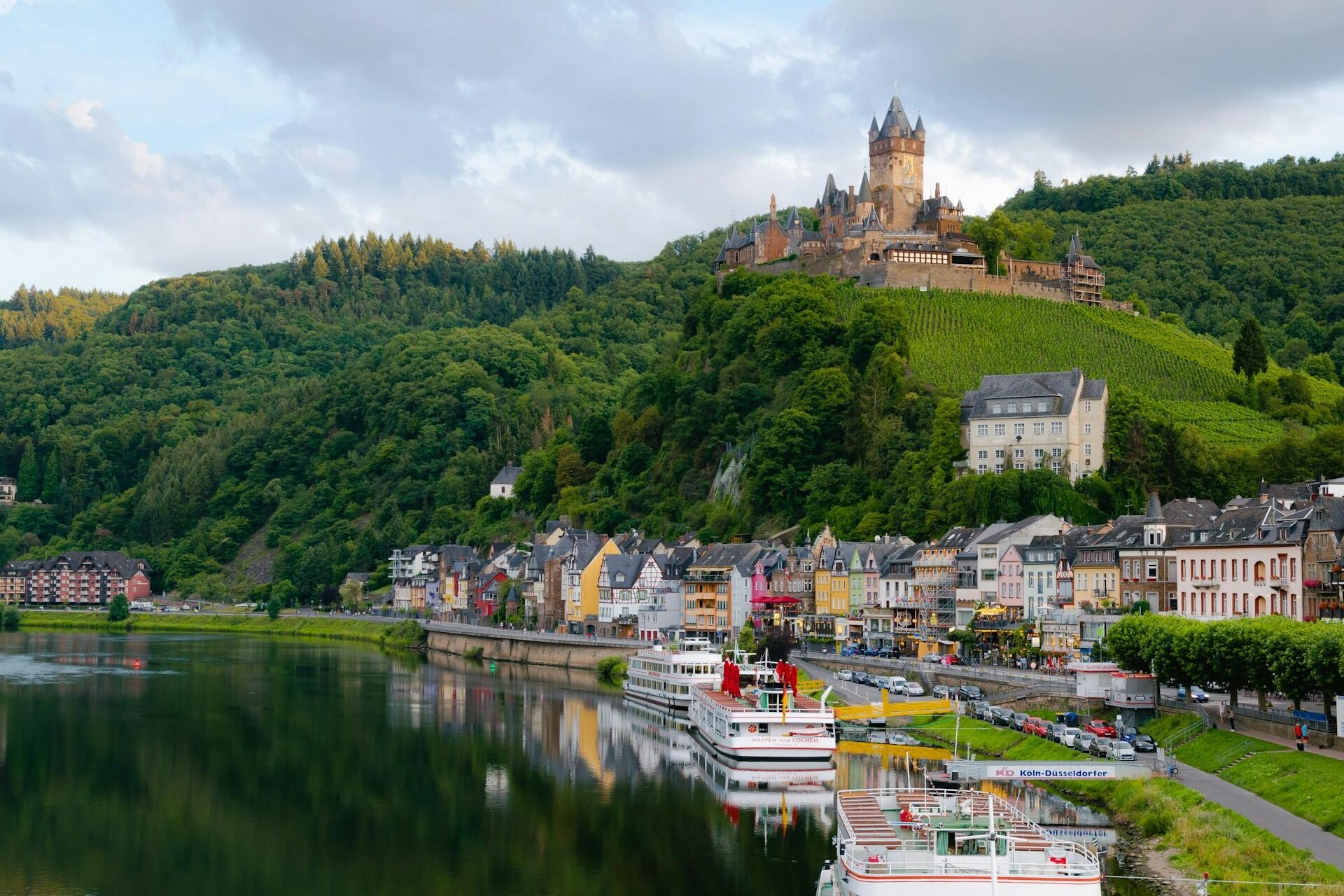 Riverside town with colourful buildings, boats and a castle on a hill