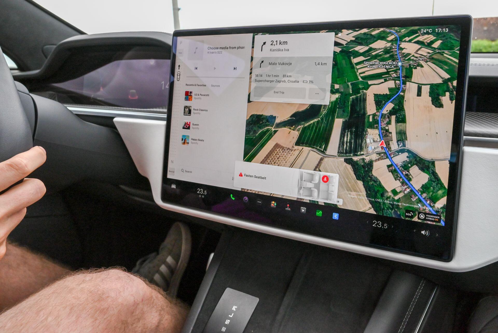 Car dashboard touchscreen displaying GPS navigation with a route overlaid on a satellite map of rural fields, alongside media controls and climate information.