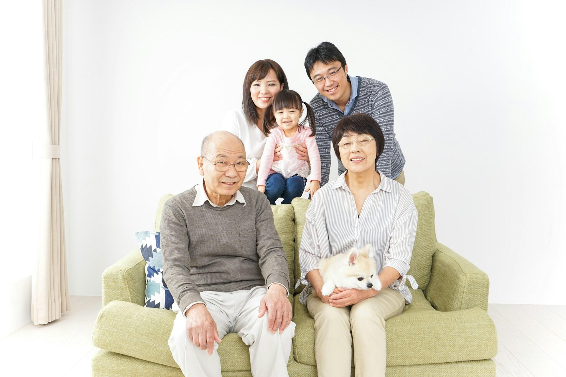 A korean family with grandparents seated, parents behind them and a baby in between the parents.