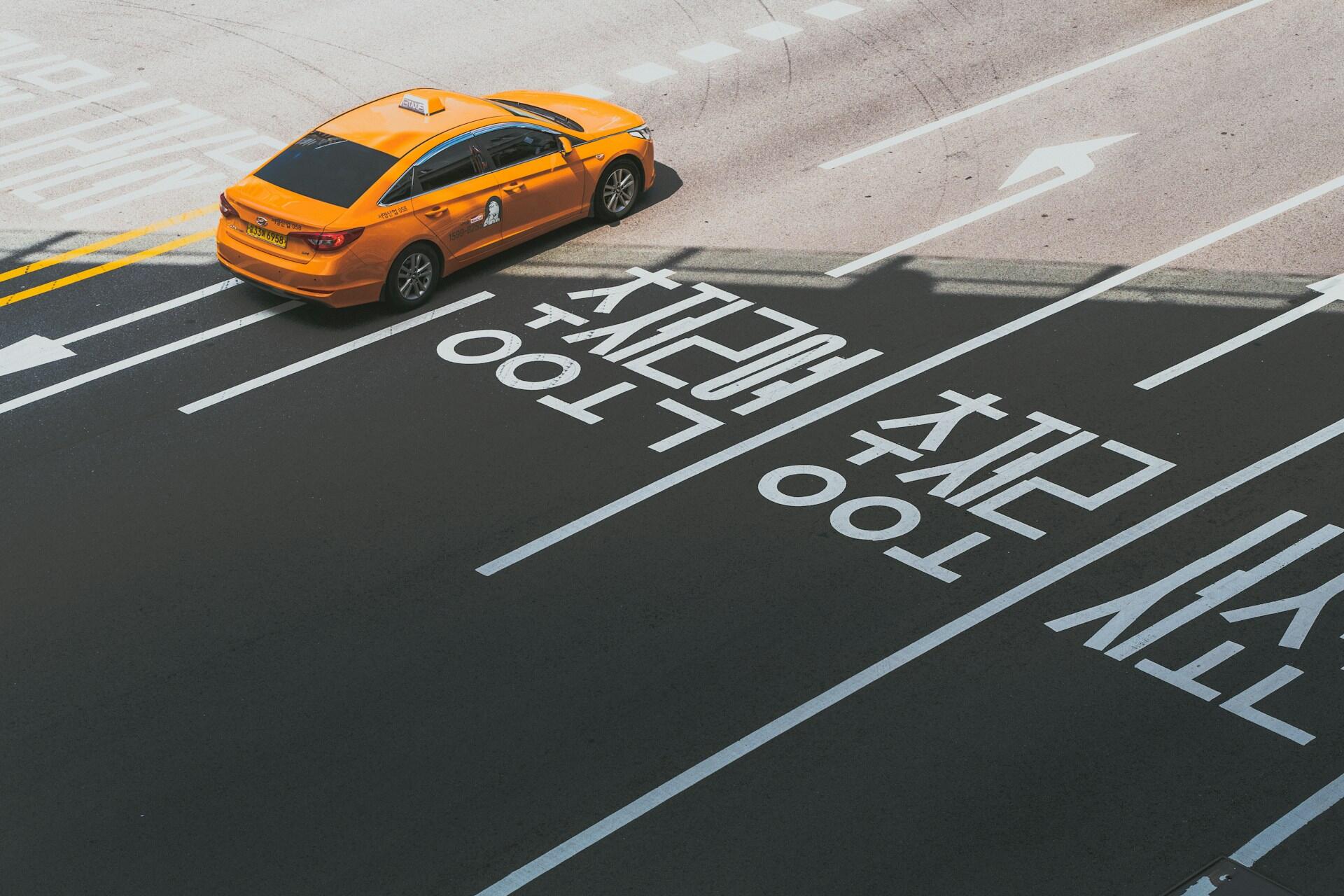 A broad road with Korean writing in each lane and a yellow taxi in the farthest one,