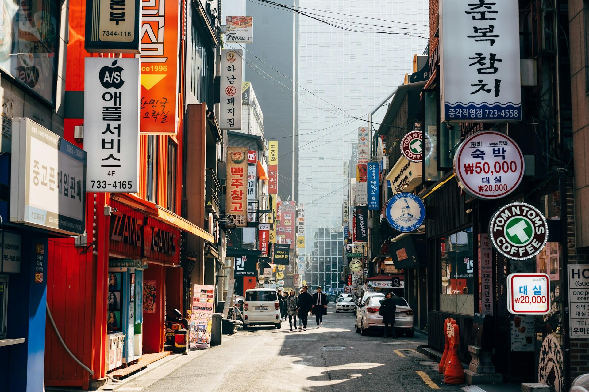 A narrow street bedecked in signs of various colours featuring Korean writing.