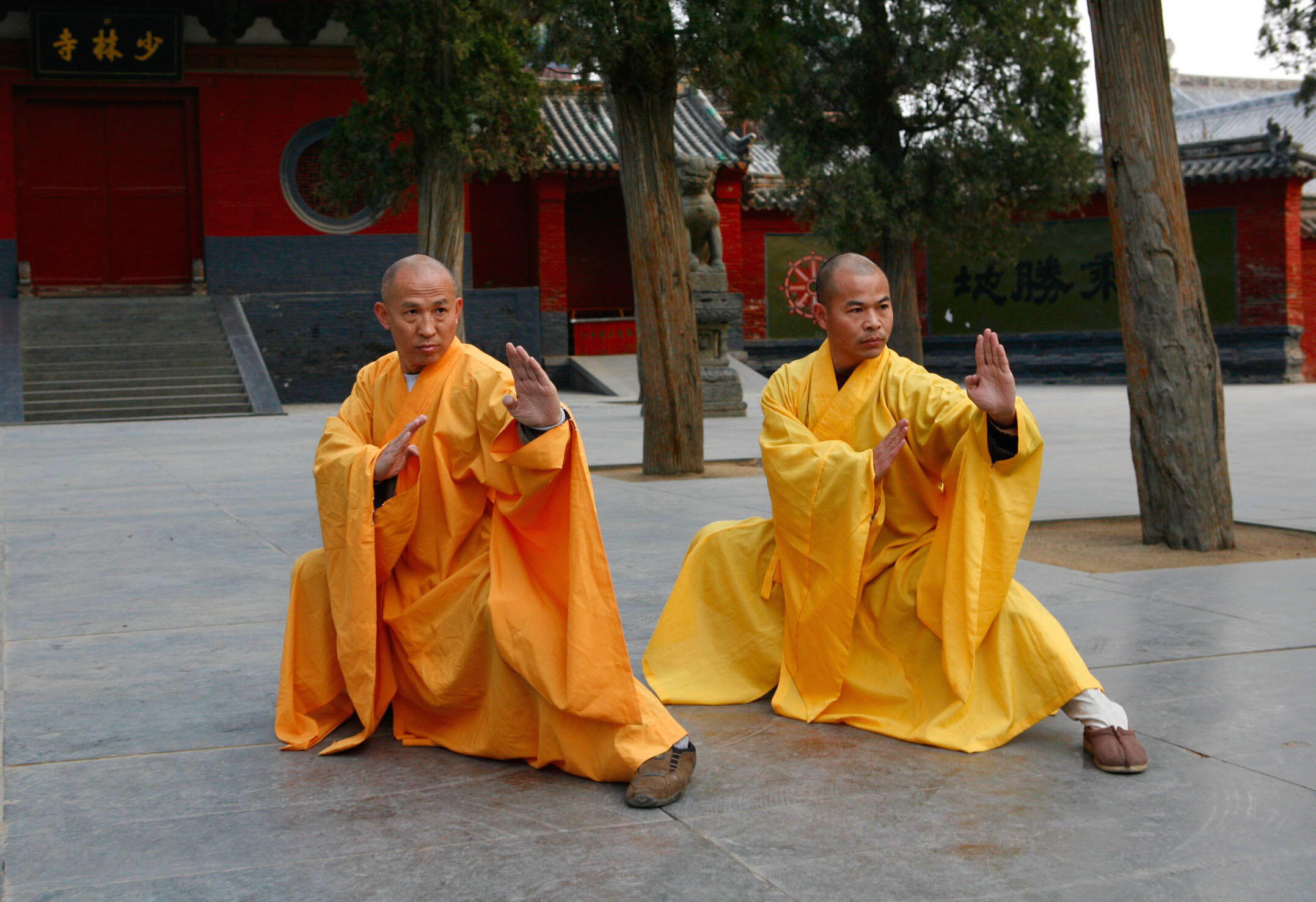 Two monks in yellow robes adopt a fighting stance in their temple's courtyard.