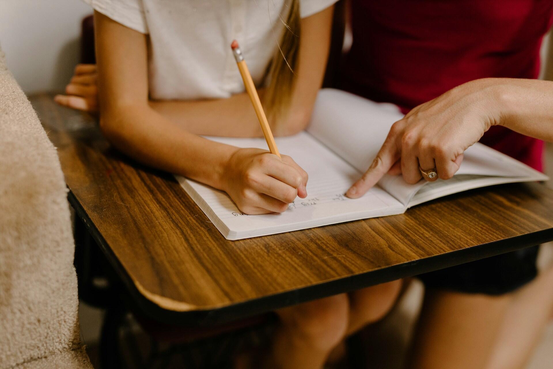 a young student working on an exercise in a notebook with a teacher giving guidance
