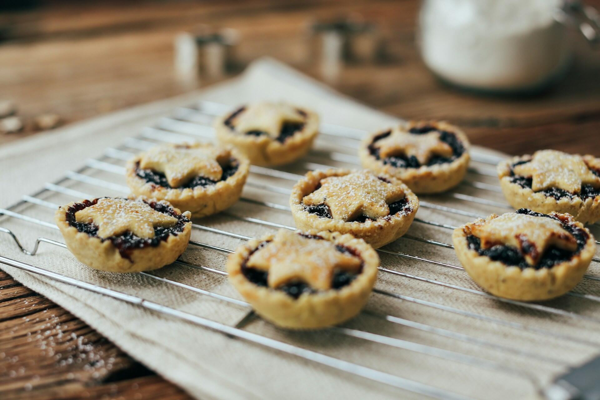 Several freshly baked mince pies with star-shaped pastry tops sit on a cooling rack.
