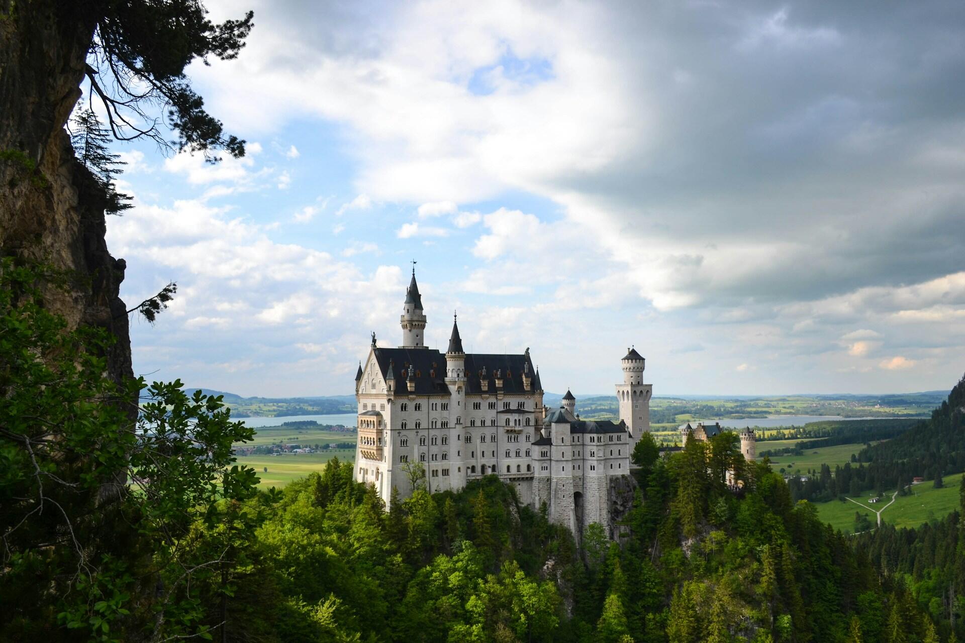 White castle surrounded by trees with mountains and clouds in the background
