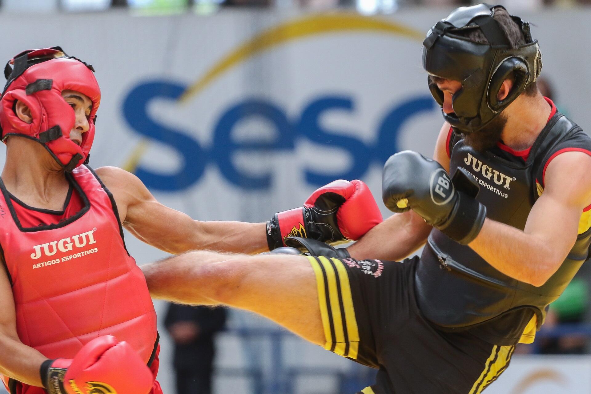 Two people wearing athletic clothing and protective gear engage in a boxing match in front of spectators.