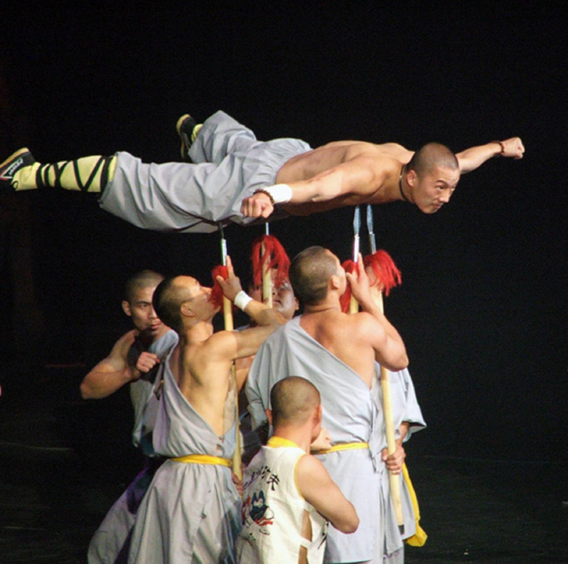 A bare-chested man wearing white trousers lies atop five pointed spears held up by men in monk's clothing.