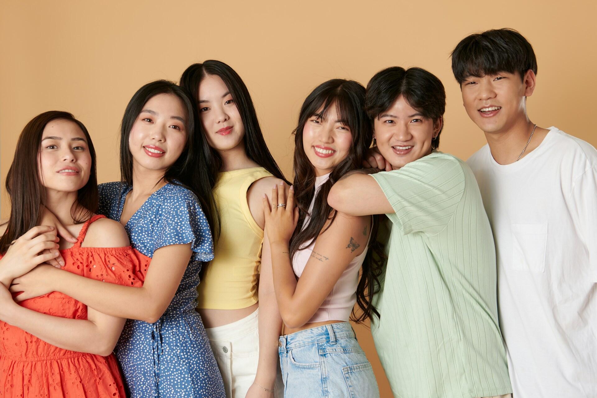Six young people smile as they pose together in front of a peach-coloured wall.