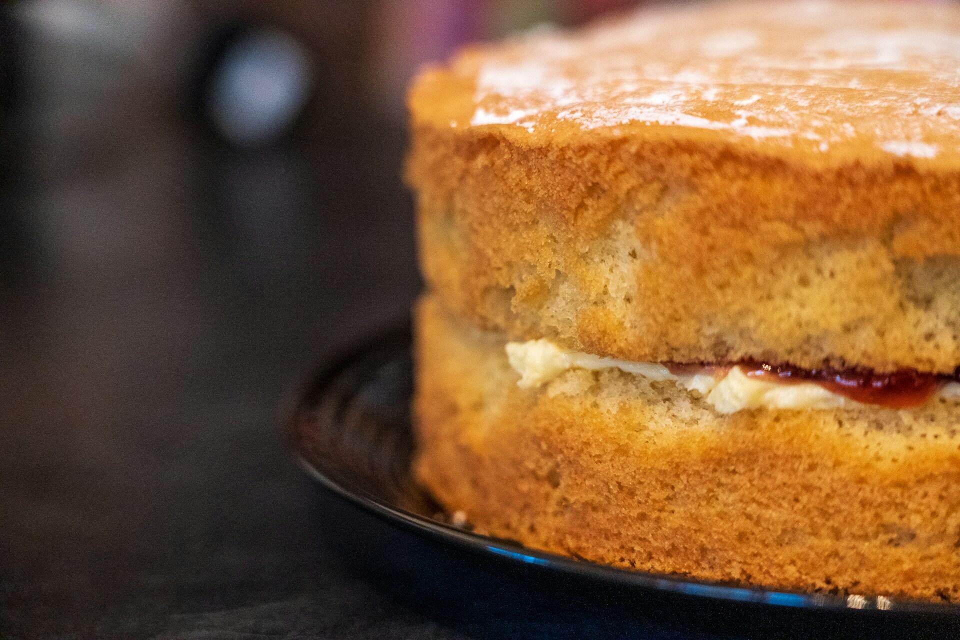 Close-up of a sponge cake with cream and jam filling dusted with powdered sugar on a black plate.