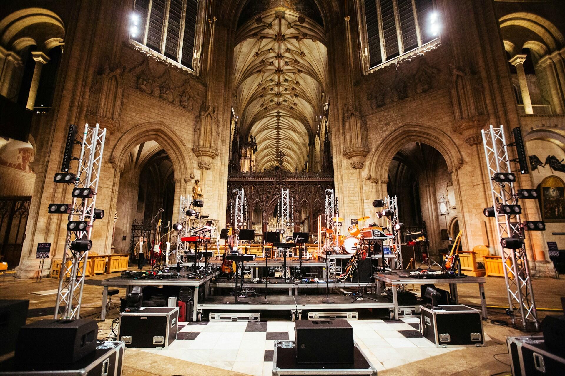 inside a large church, a stage with instruments, sound equipment, and lighting stands is arranged