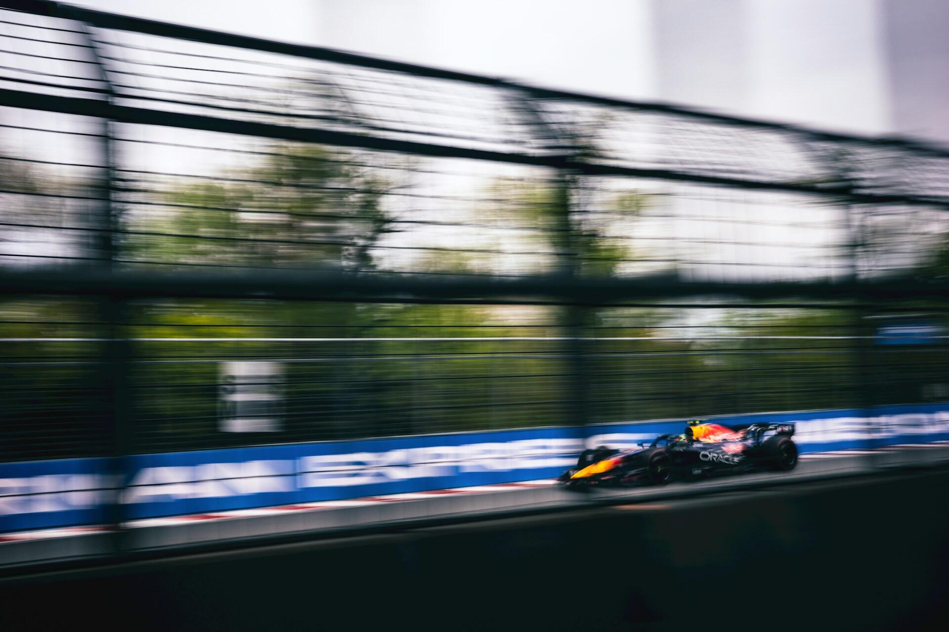 Blurred image of a Red Bull Formula 1 car speeding on a racetrack with safety fencing and advertising banners in the background.