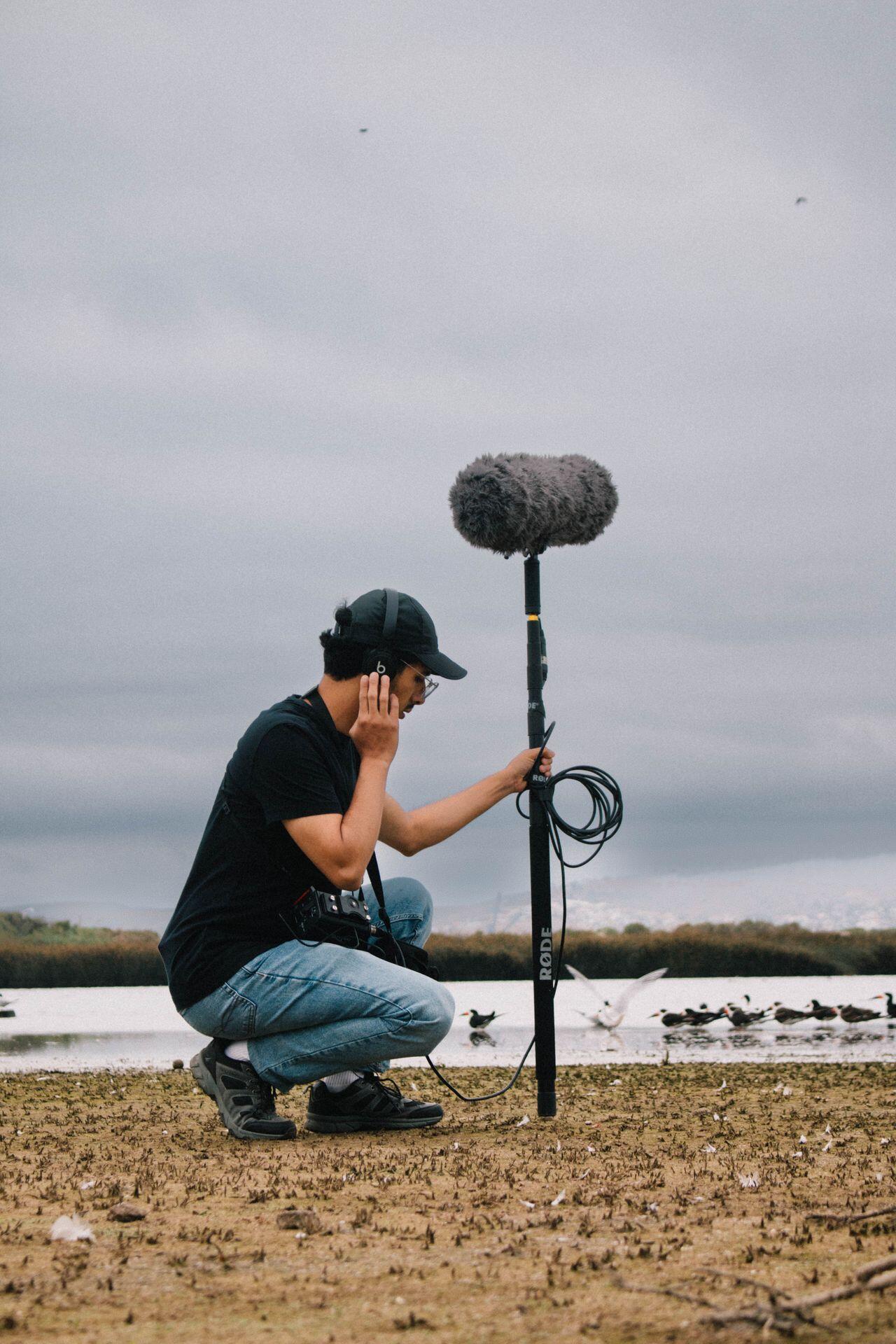 field sound technician recording beach and seagull sounds on location using a large boom mic with a thick wind muff