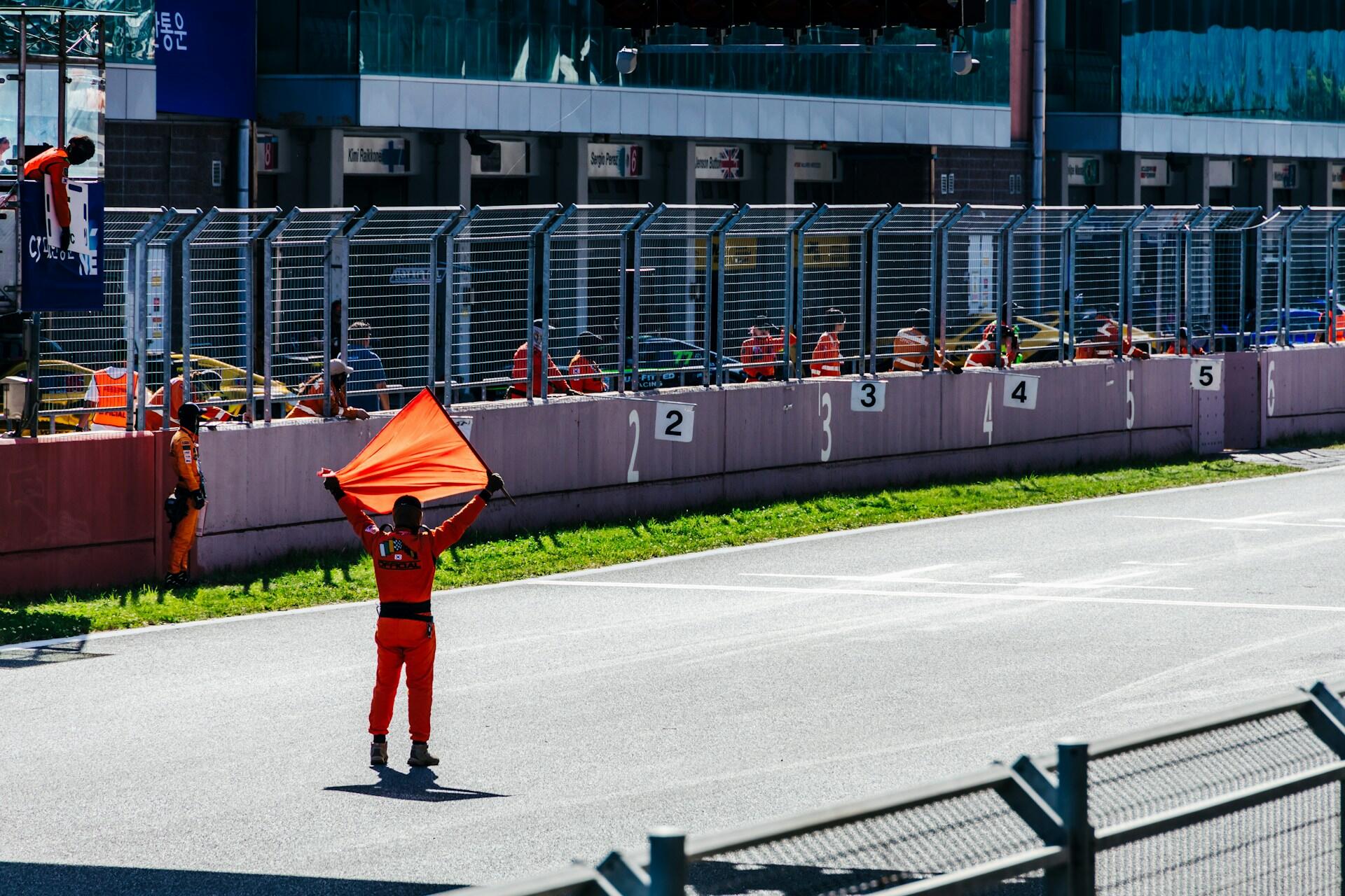 A man stands holding an orange flag, displaying it prominently against a neutral background.