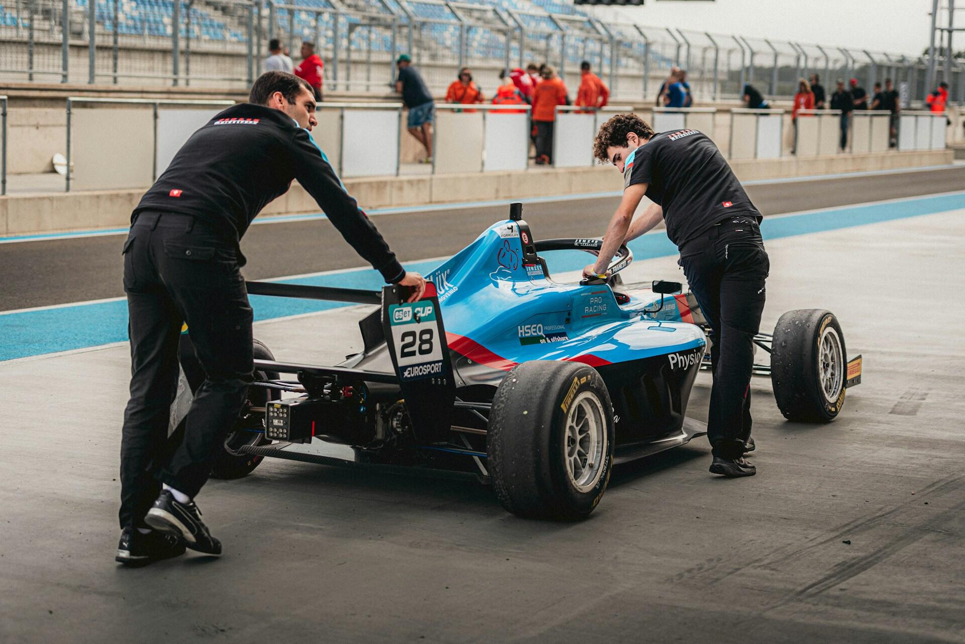 Two men are collaborating on the maintenance of a racing car in a workshop setting.