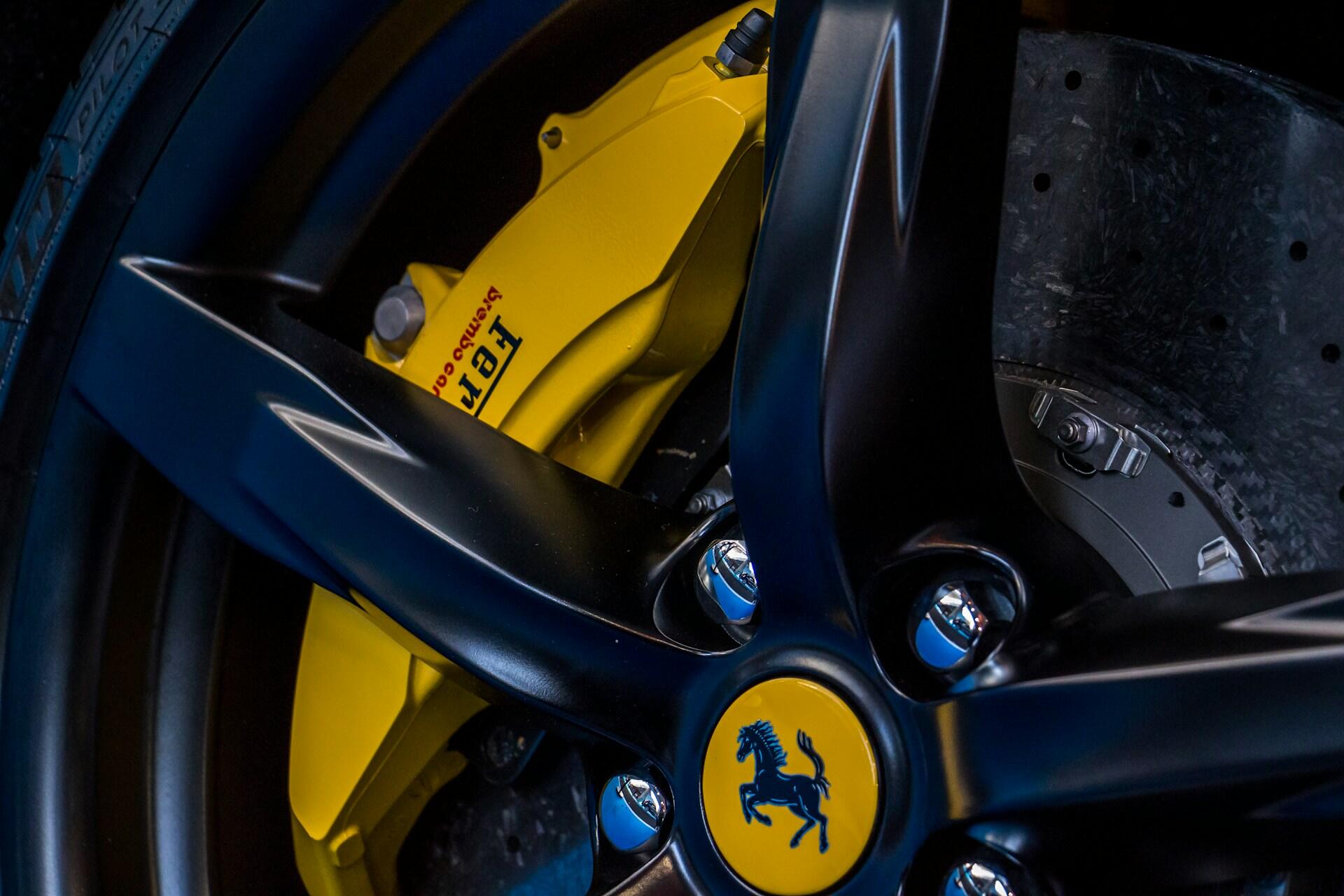 Close-up of a black Ferrari wheel with yellow Brembo brake caliper and brake disc visible behind the spokes.