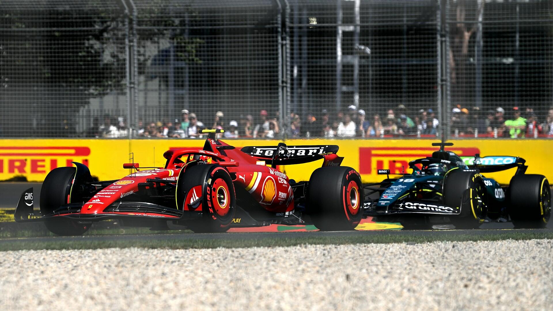 Two Formula 1 cars, one red Ferrari and one black Aston Martin, race closely on a track near a yellow Pirelli advertisement.