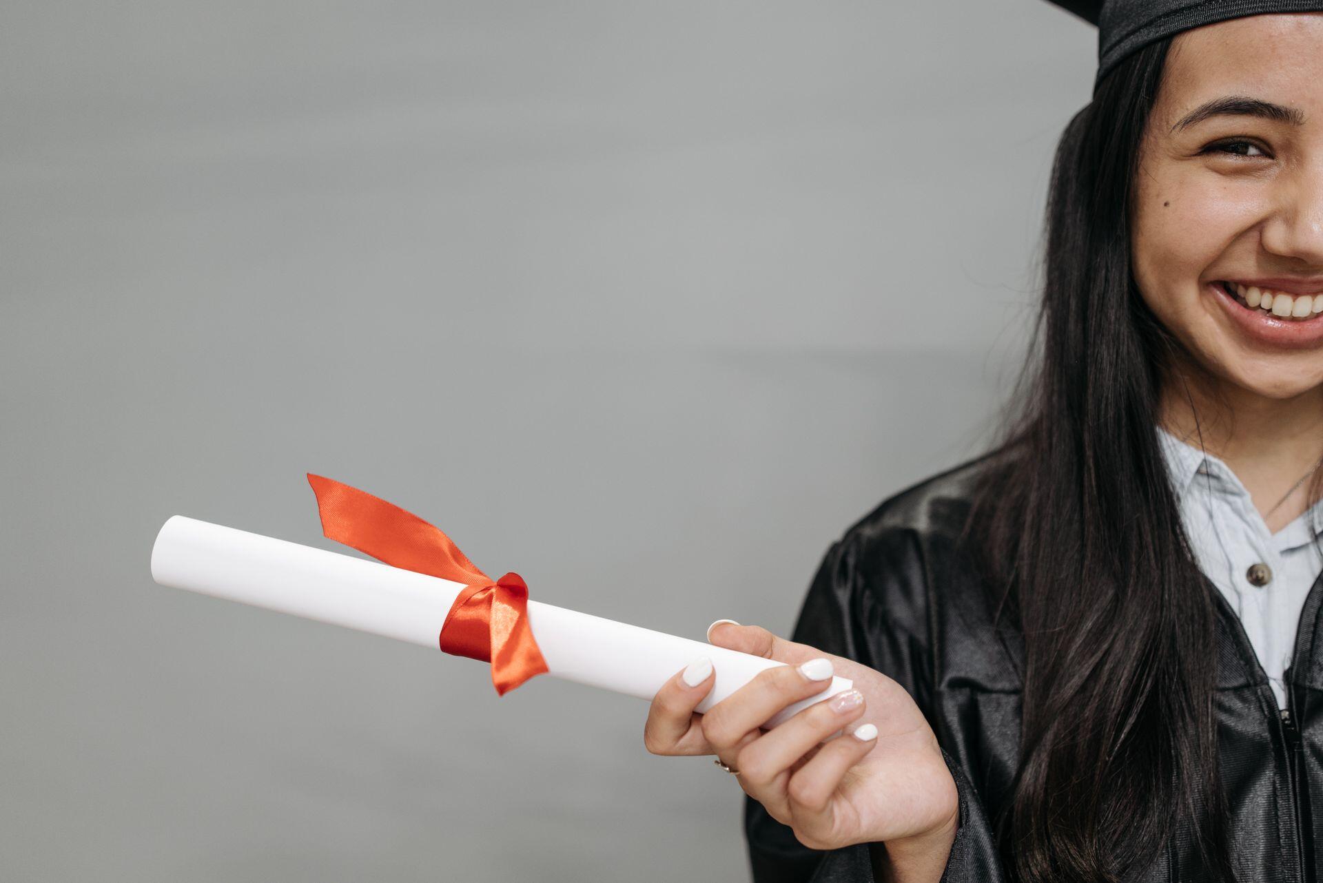 Female student in graduation attire holding up a degree fixed with a ribbon