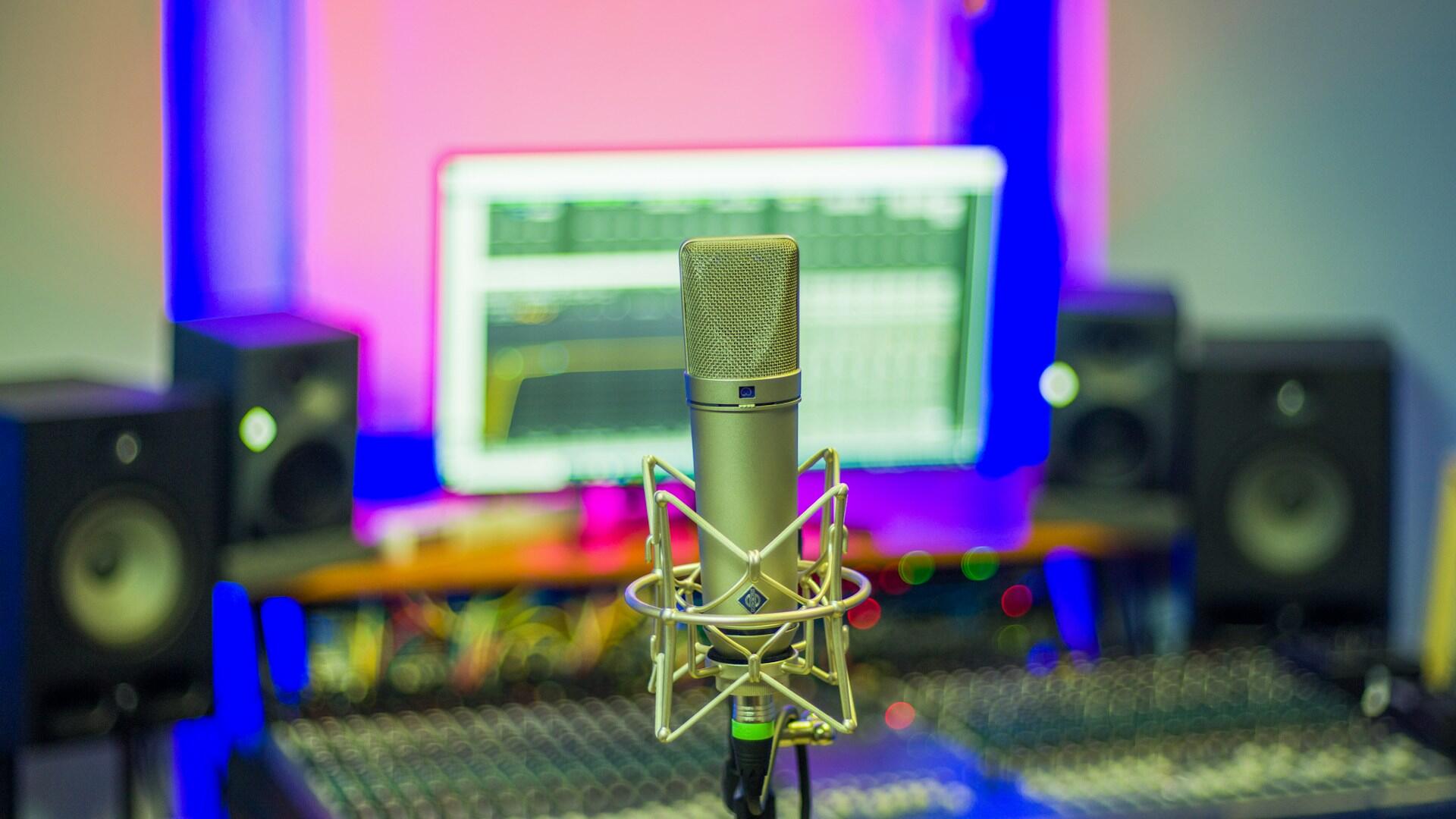 microphone in a stand in a casual home studio with a computer monitor displaying a DAW in the background