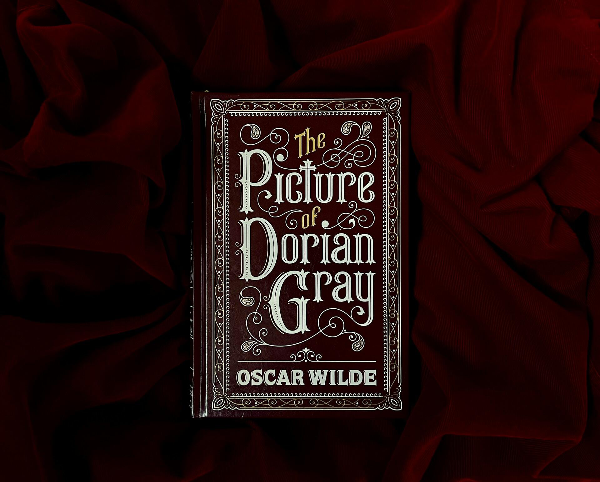 A decorative book titled “The Picture of Dorian Gray” by Oscar Wilde lies on dark red fabric.