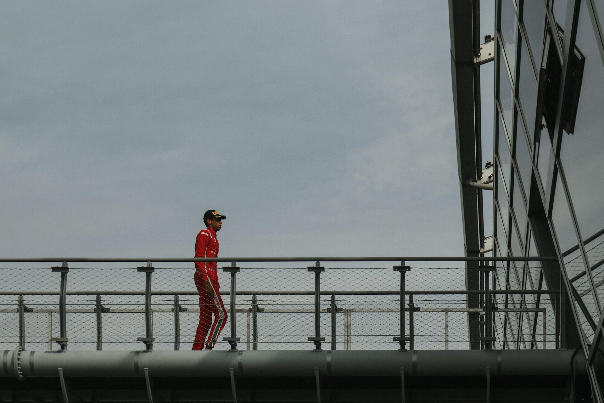 A man in a red suit stands confidently on a bridge, overlooking the scenery around him.