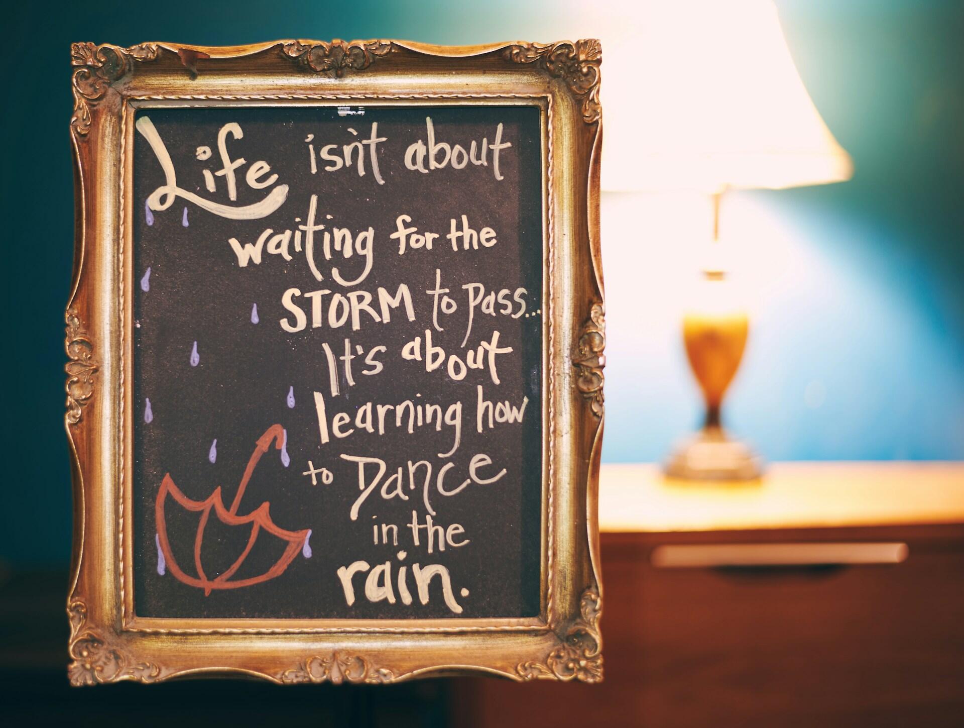 A chalkboard in a golden frame with a positive life quote written in light brown chalk.
