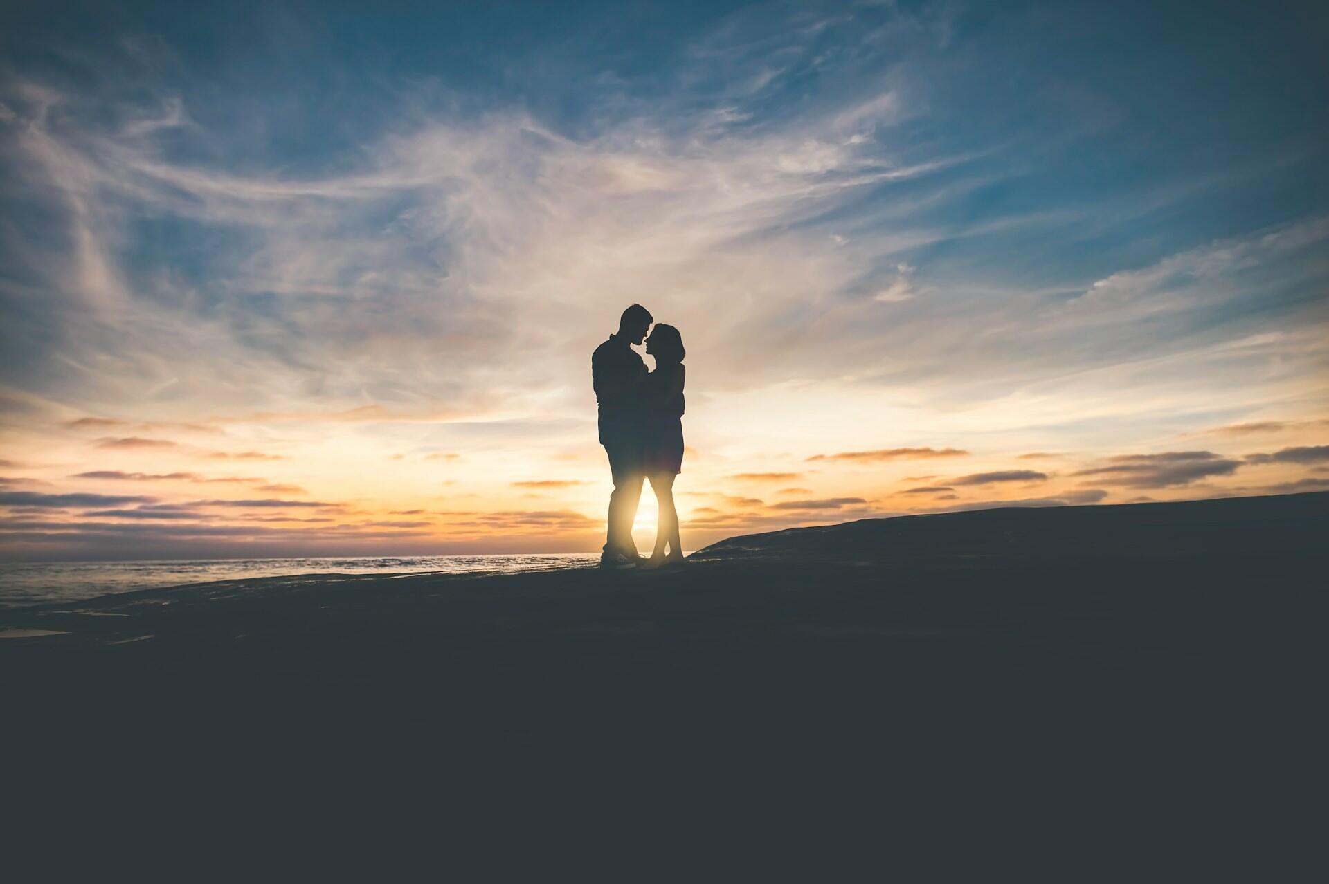 A couple kissing on the beach at sunset, creating a beautiful silhouette against the colourful sky.