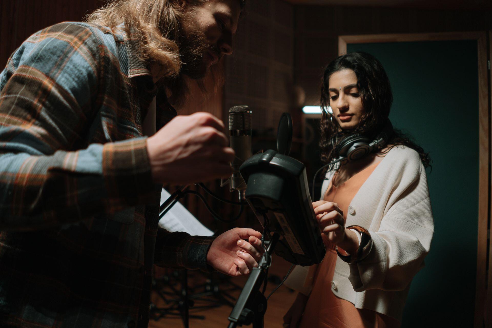 a recording engineer helps adjust a singer's microphone in the recording studio