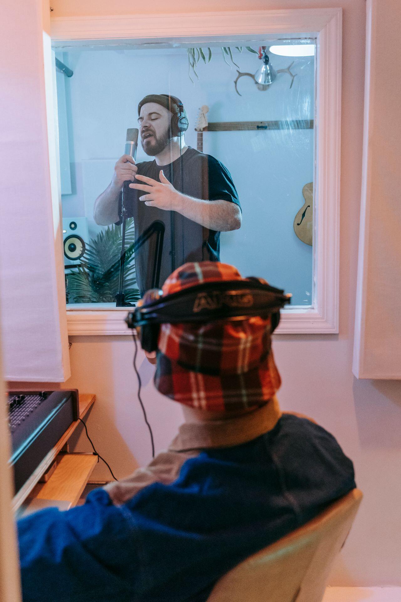 recording engineer in the audio booth, listening to a singer in the recording studio in the next room, separated by a large window