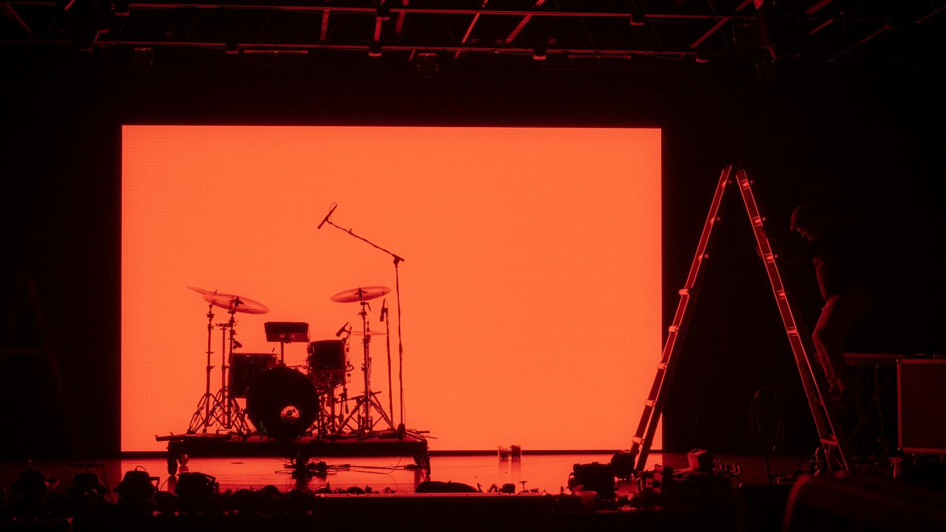 a lighting engineer works on installing and adjusting stage lights over a drum set in a concert venue