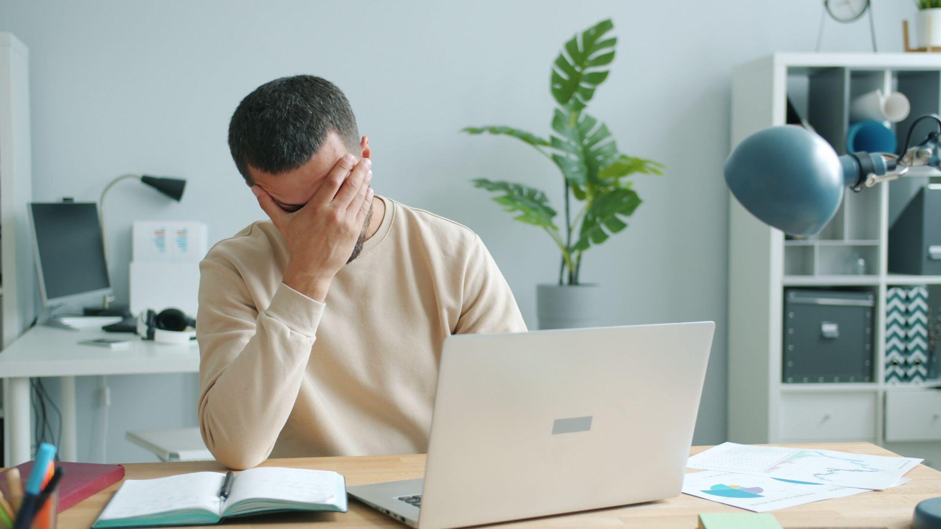 Man holding his head in his hand while sat at desk