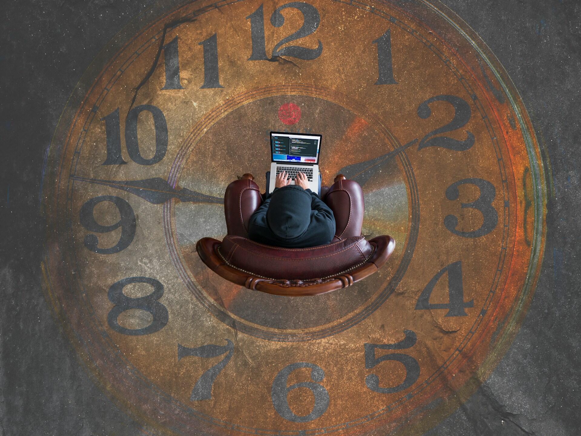 A person sits in a brown armchair in the middle of a large sepia-toned and black clock, working on a computer.