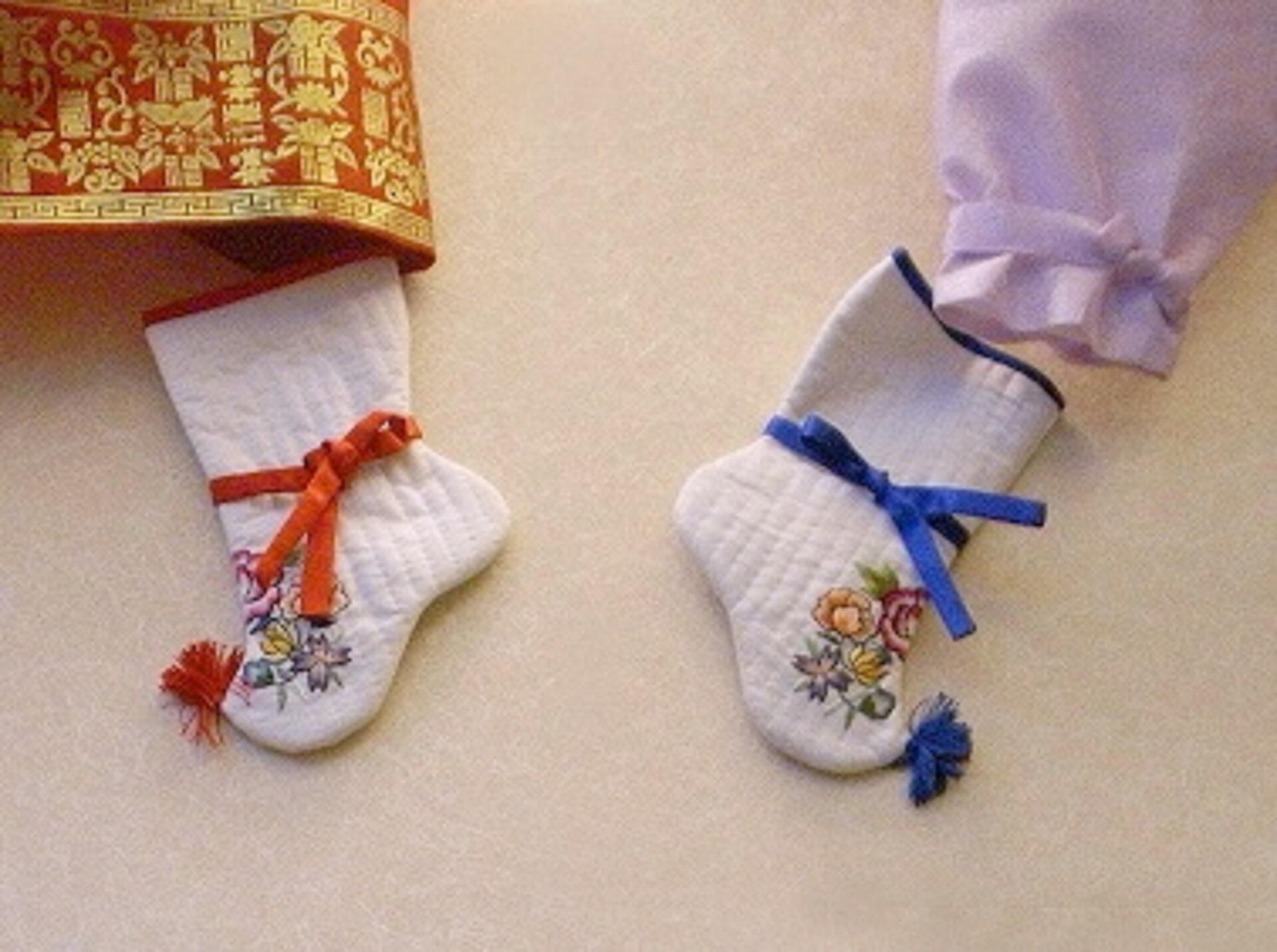 Two socks, one with red trimming and the other with blue, like close to other traditional Korean garb.