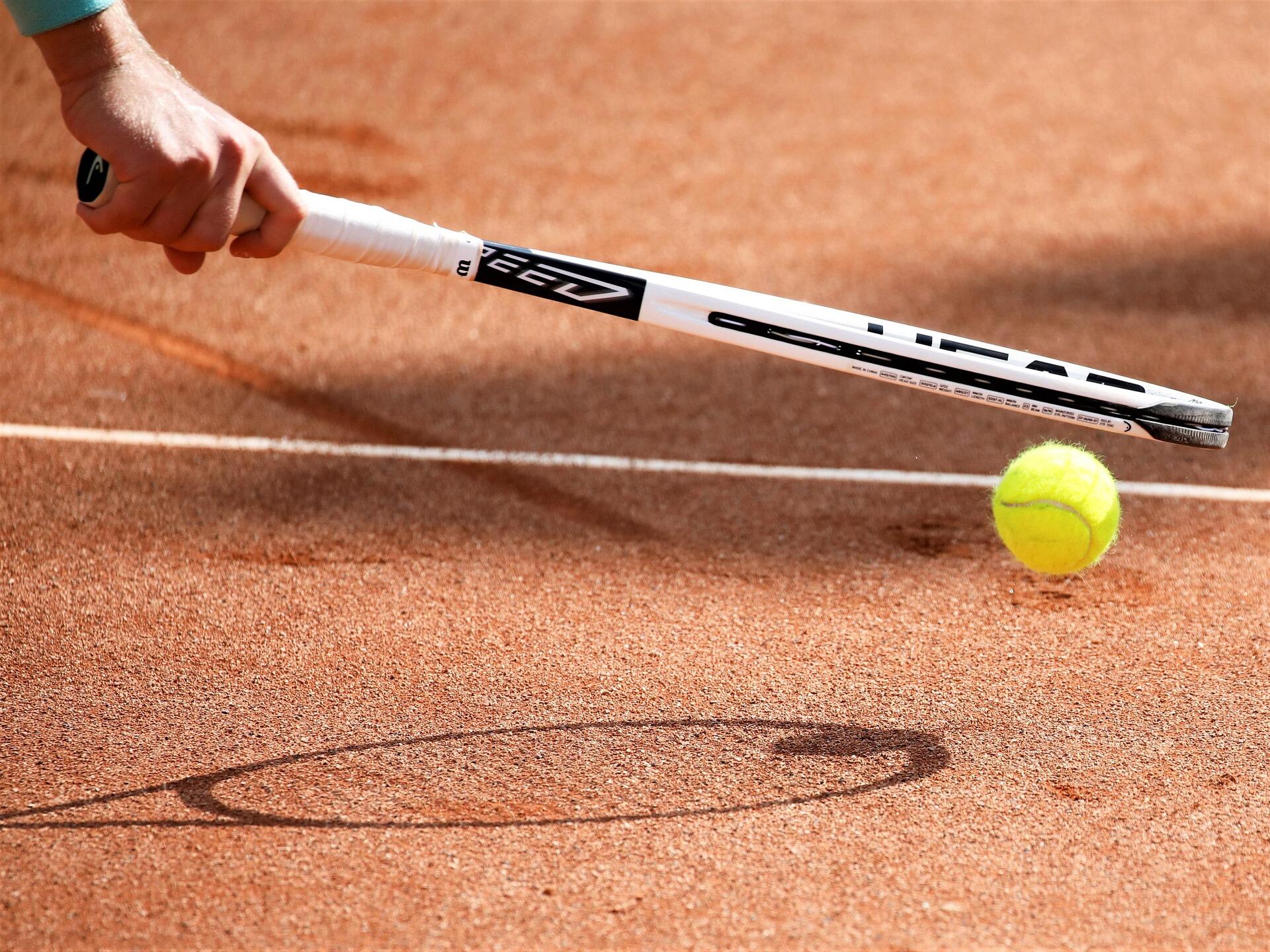 Person holding racket bouncing ball up and down on clay court surface