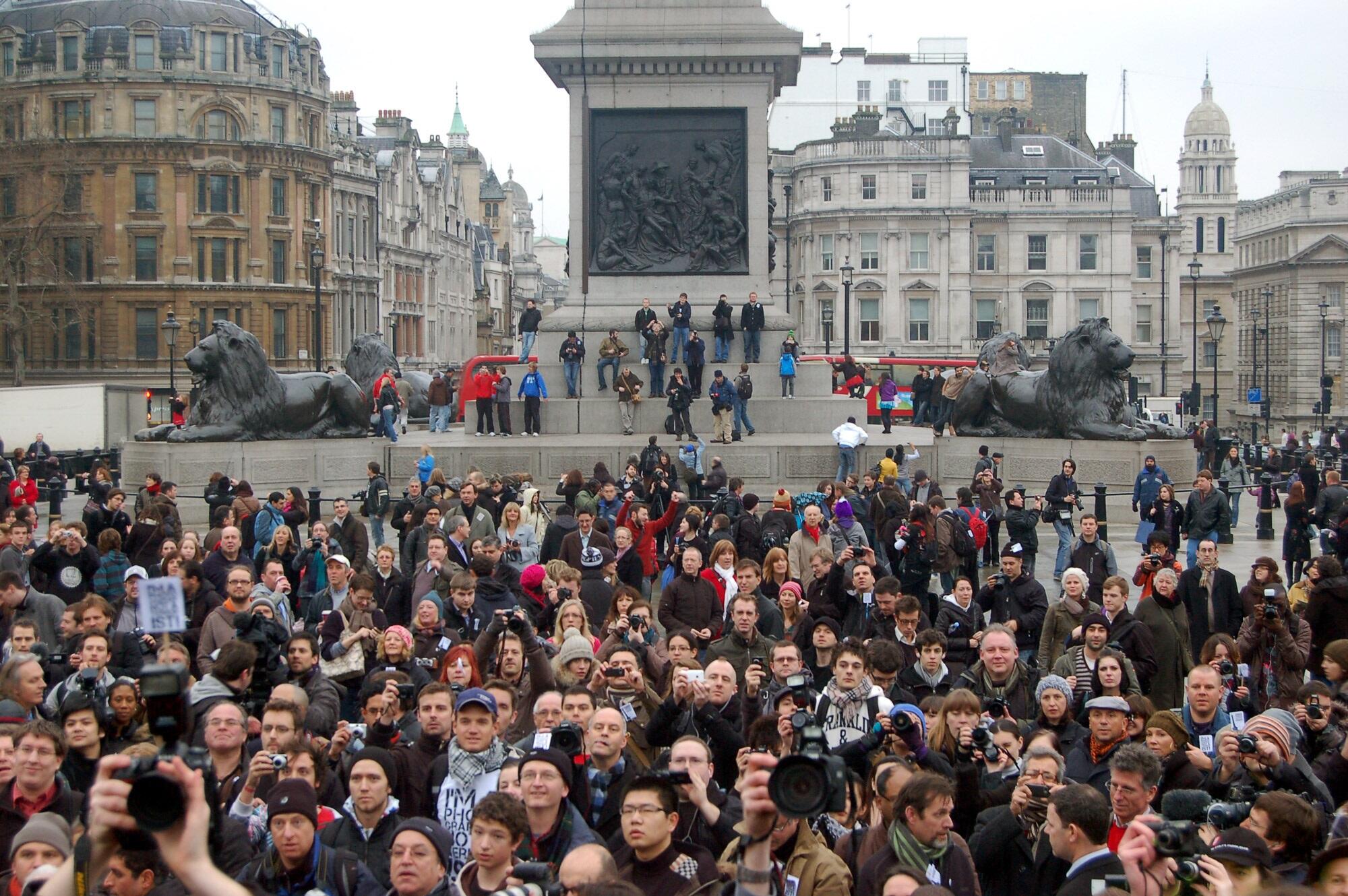A crowd of people in front on a white granite statue in an open outdoors space on a cloudy day.