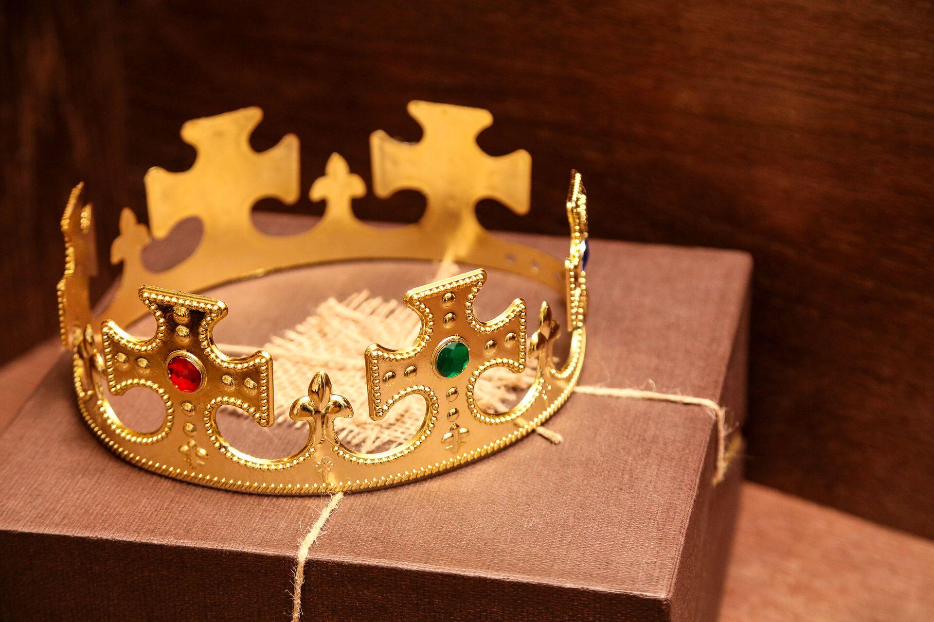 A gold decorative crown with red and green gemstones rests on a brown fabric-covered box.